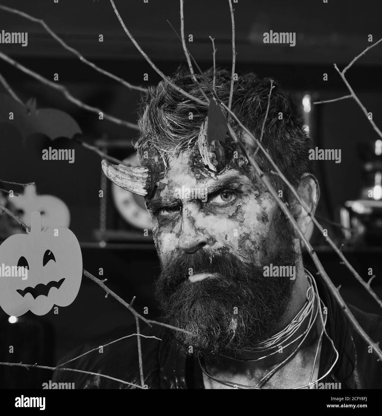 Homme portant un maquillage effrayant avec des branches, des citrouilles et des chauves-souris d'Halloween sur fond. Démon avec des cornes, visage mauvais et sang séché sur les cheveux. Diable ou monstre de la fête. Concept de fête de costume d'Halloween Banque D'Images
