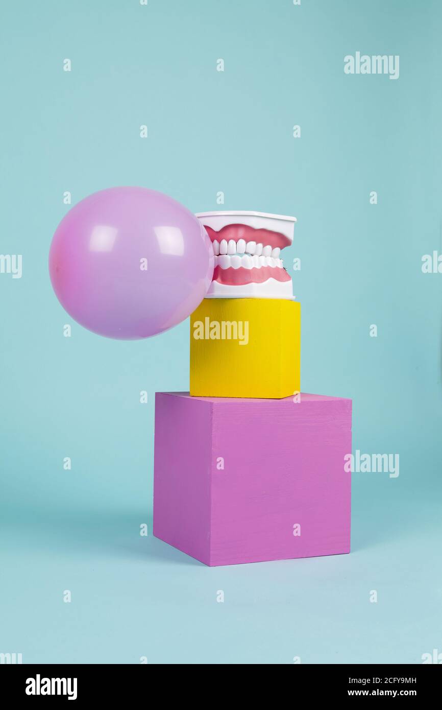 un modèle anatomique de dent en plastique pour apprendre à brosser les dents en tenant une boule de gomme à mâcher sur des cubes colorés. Humour et ambiance pop. Minimale Banque D'Images