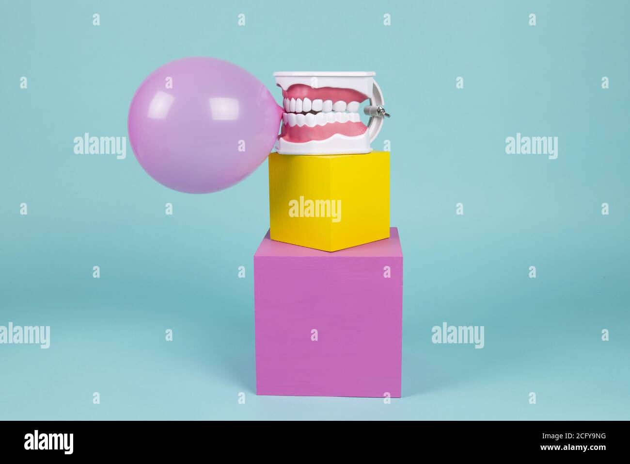 un modèle anatomique de dent en plastique pour apprendre à brosser les dents en tenant une boule de gomme à mâcher sur des cubes colorés. Humour et ambiance pop. Minimale Banque D'Images