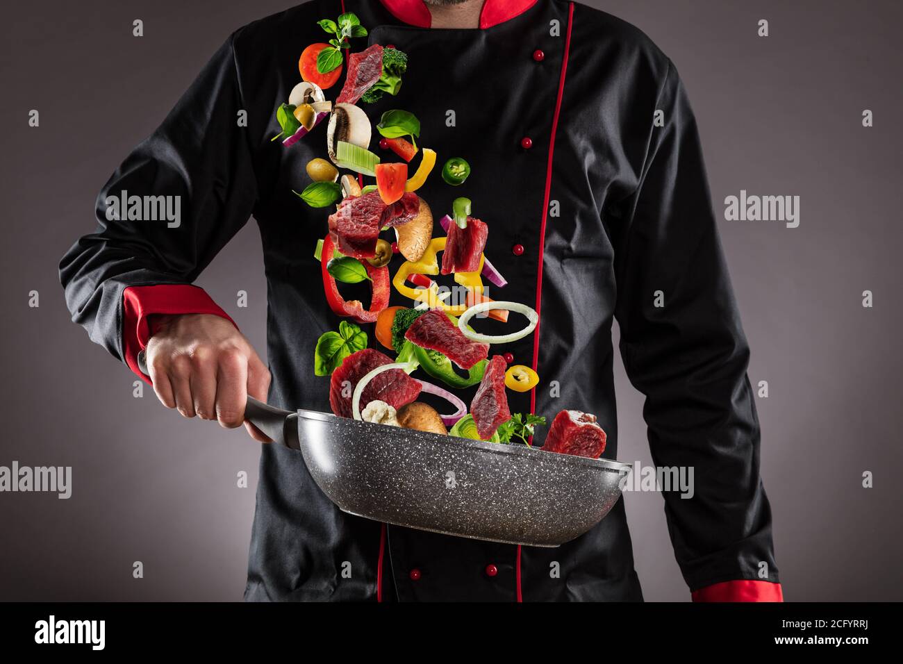 Gros plan du chef qui jette de la viande de bœuf avec des légumes dans l'air. Concept de préparation des aliments Banque D'Images