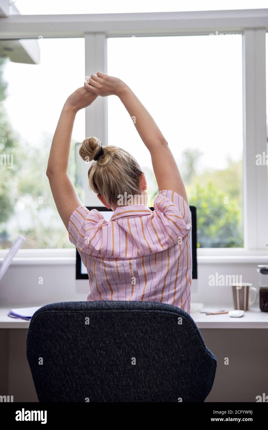 Vue arrière de la femme travaillant à domicile sur l'ordinateur dans Bureau à domicile s'étirant au bureau Banque D'Images