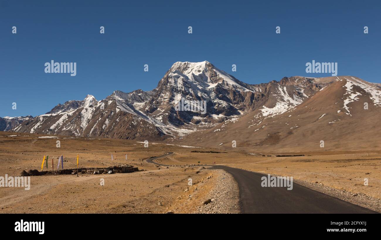 Image de mise au point sélective d'une longue route solitaire avec des courbes sur le plateau tibétain avec des montagnes enneigées et des sommets et ciel bleu clair devant et la tibe Banque D'Images