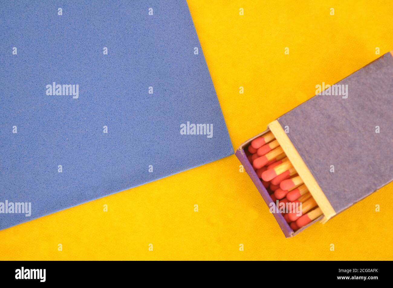 Boîte d'allumettes, en bois, allumettes à tête rouge dans une boîte à moitié ouverte, sur fond bleu et jaune, avec espace de copie Banque D'Images