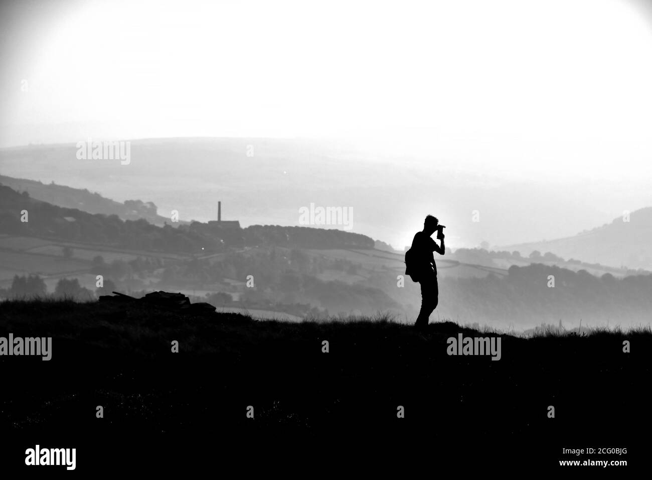 Photographe silhoueté au-dessus de la vieille ville et du pont Hebden, Pennines, Yorkshire Banque D'Images