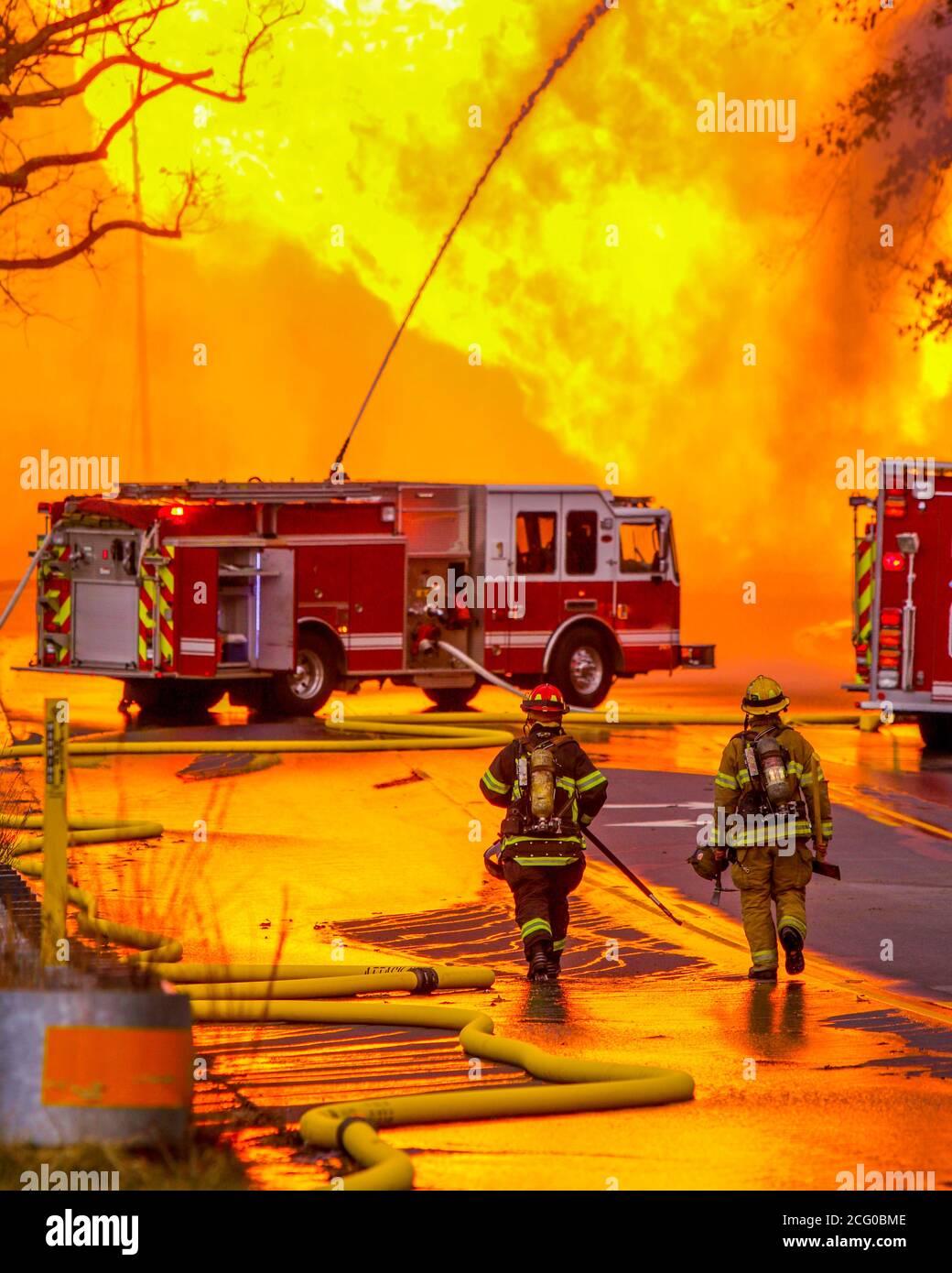 Deux premiers intervenants de la caserne de pompiers locale se rendent vers un moteur d'incendie contrôlant un incendie massif d'une éruption de ligne de gaz naturel. Banque D'Images