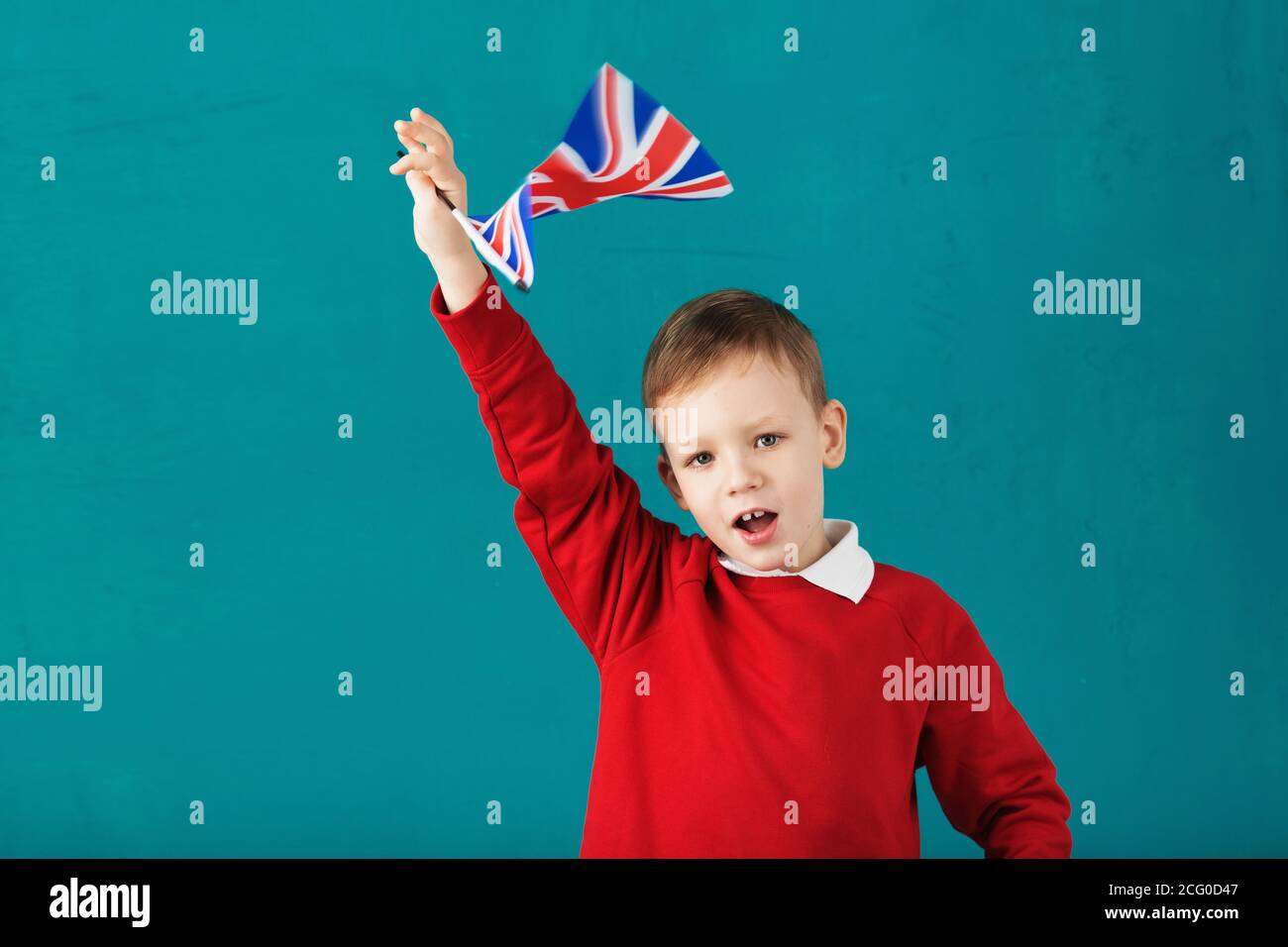 Vacances scolaires en Grande-Bretagne. Petit écolier avec le drapeau national du Royaume-Uni ayant du plaisir contre le mur bleu. Anglais pour enfants con Banque D'Images