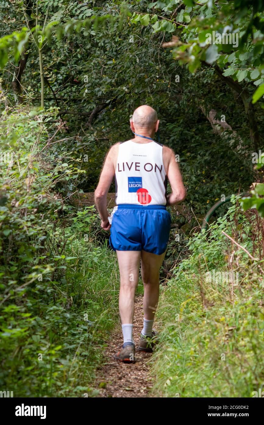 Homme senior marchant sur un sentier campagnard portant un gilet d'exercice, un short et des chaussures de course à pied Banque D'Images