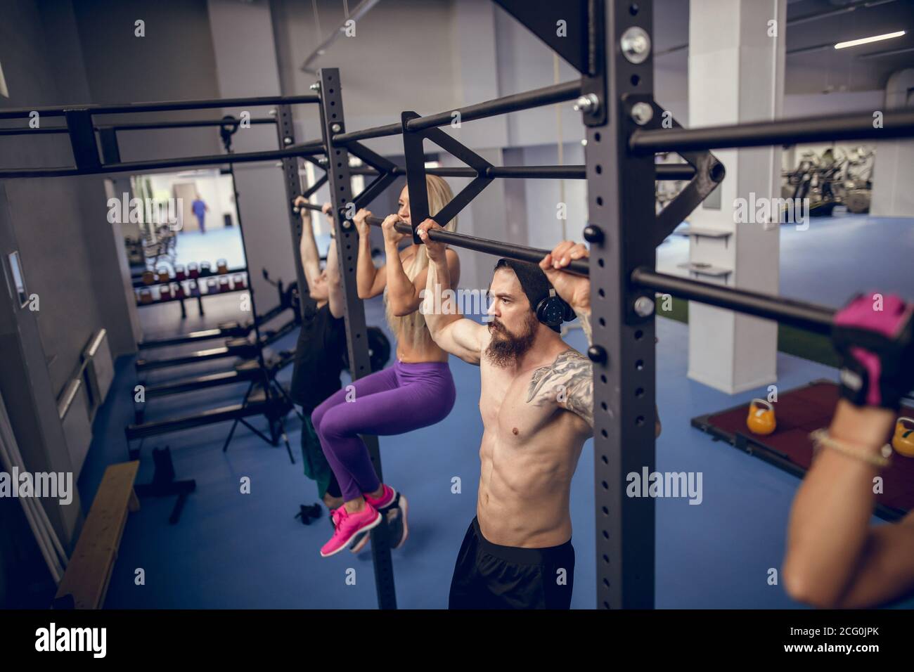 Groupe de jeunes hommes et femmes adultes attirants faisant tirer ups sur le bar dans la salle de sport d'entraînement de cross-fit avec la brique murs et tapis noirs Banque D'Images