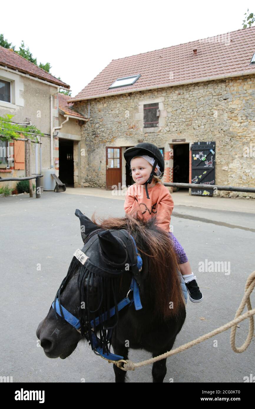 Petite fille poney à cheval dans une écurie, France Banque D'Images