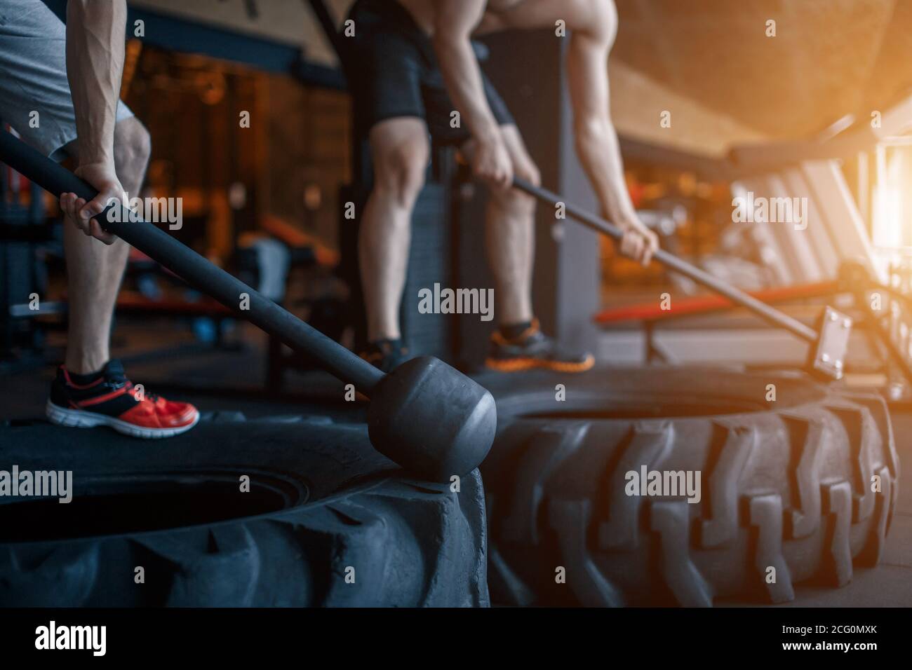 Deux jeunes hommes avec un marteau frappe sur un pneu dans la salle de gym. Entraînement. Banque D'Images