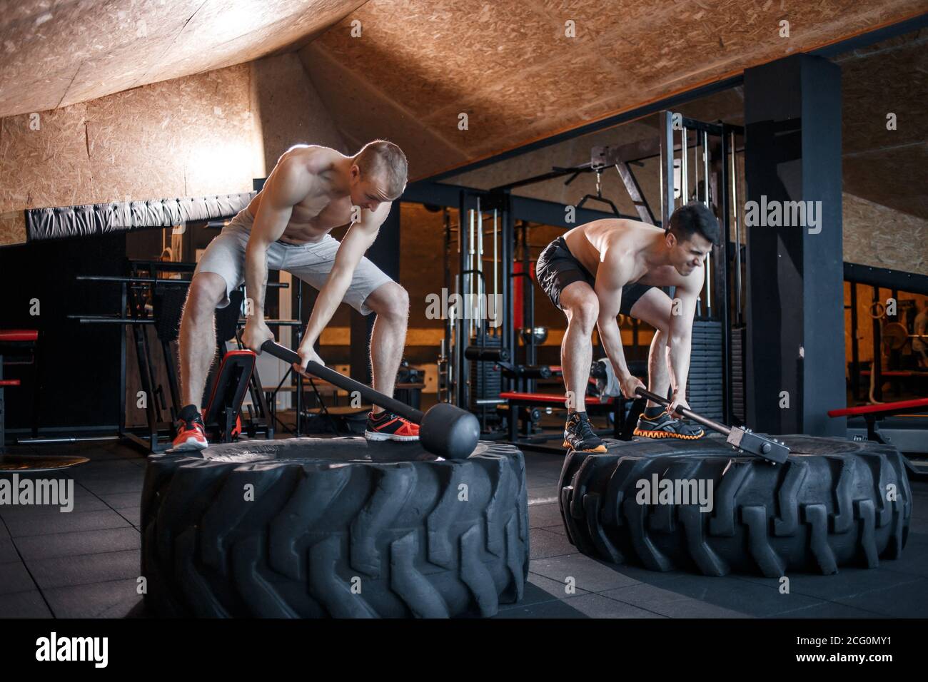 Deux jeunes hommes avec un marteau frappe sur un pneu dans la salle de gym. Entraînement. Banque D'Images