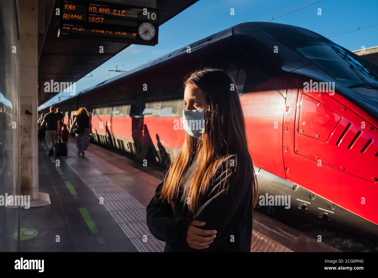 Une adolescente âgée de 13 ans vérifie l'horaire de départ à la gare de Venise (Italie). Elle porte des vêtements décontractés et un masque chirurgical. Banque D'Images
