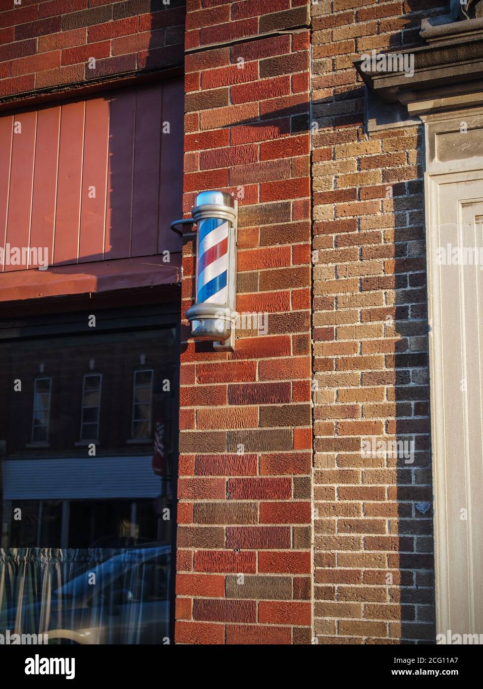 Un poteau de barbier traditionnel rouge, blanc et bleu à l'extérieur d'un bâtiment en brique dans une petite ville américaine. Banque D'Images