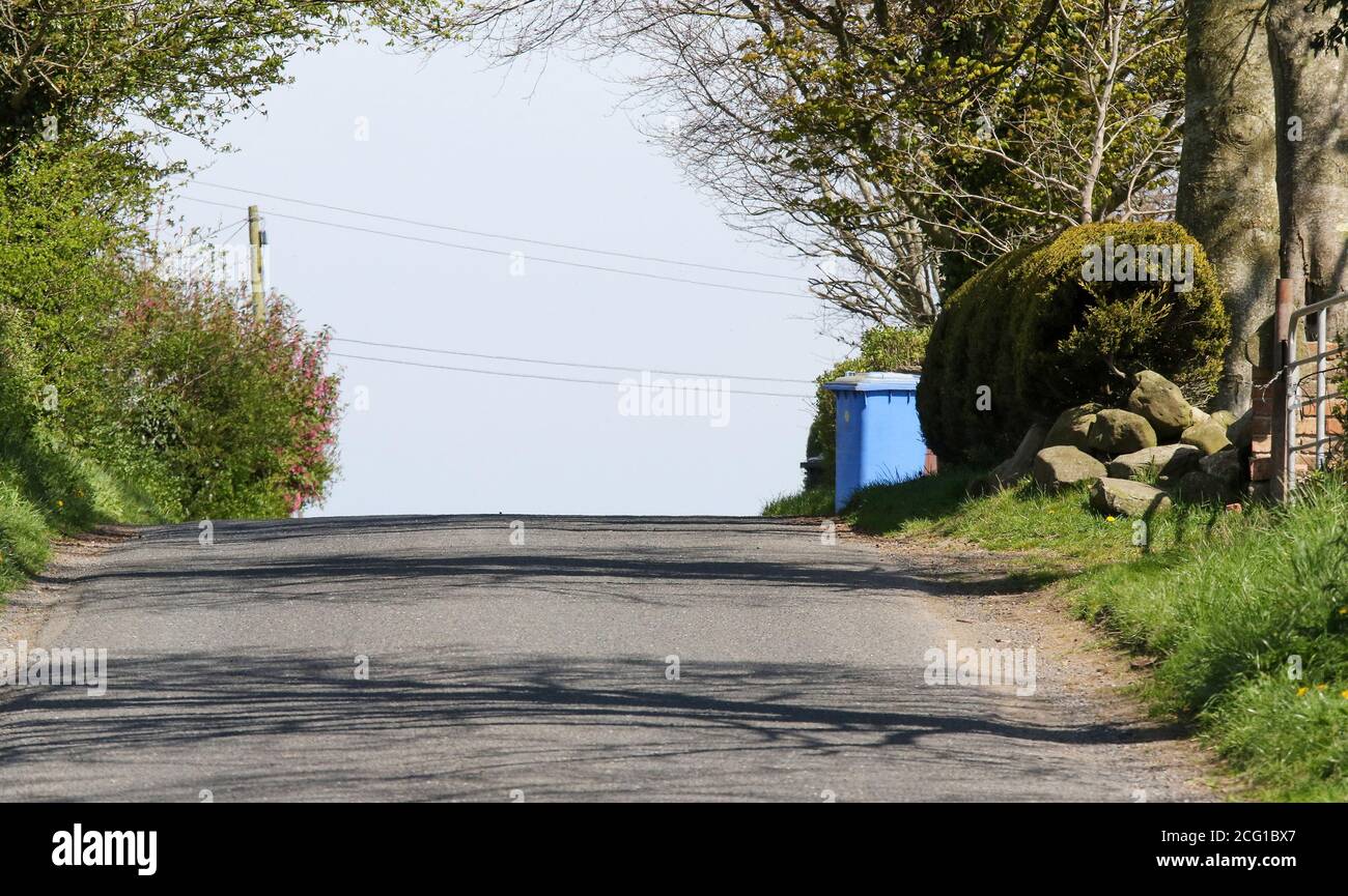 Poubelle à roulettes UK Blue en attente de collecte sur le bord de la route, sur une colline, sur une route rurale en Irlande du Nord, le jour ensoleillé du printemps. Banque D'Images