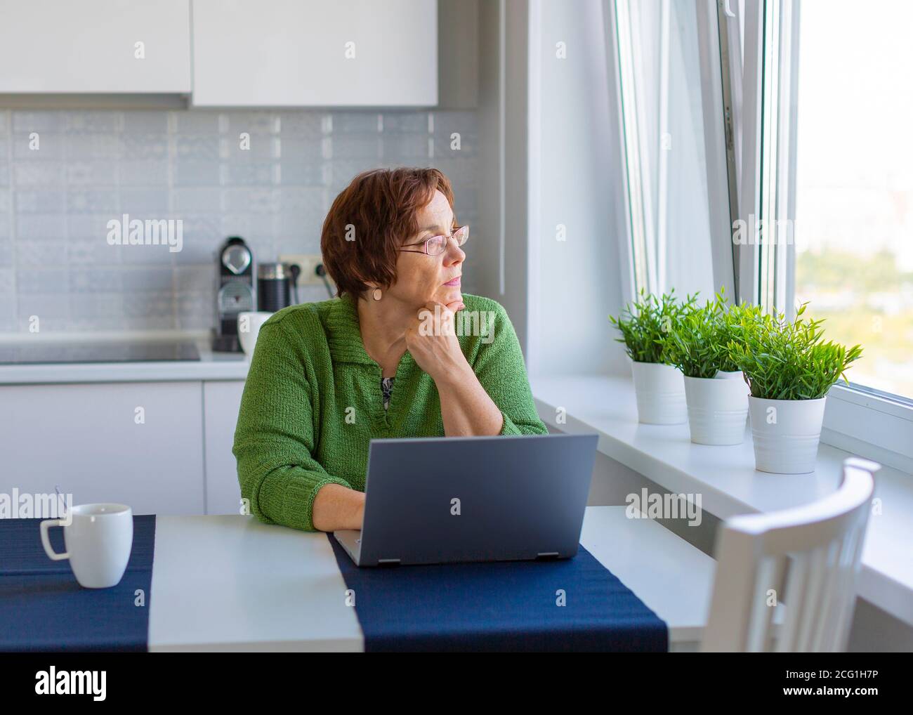 Femme sénior et attentionnés travaillant à la maison avec un ordinateur portable. Elle regarde loin. Banque D'Images