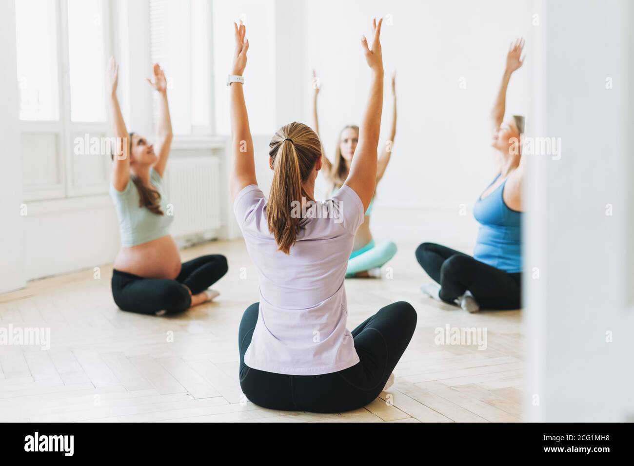 Groupe de femmes enceintes en uniforme de sport avec entraîneur faire gymnastique en studio lumineux Banque D'Images