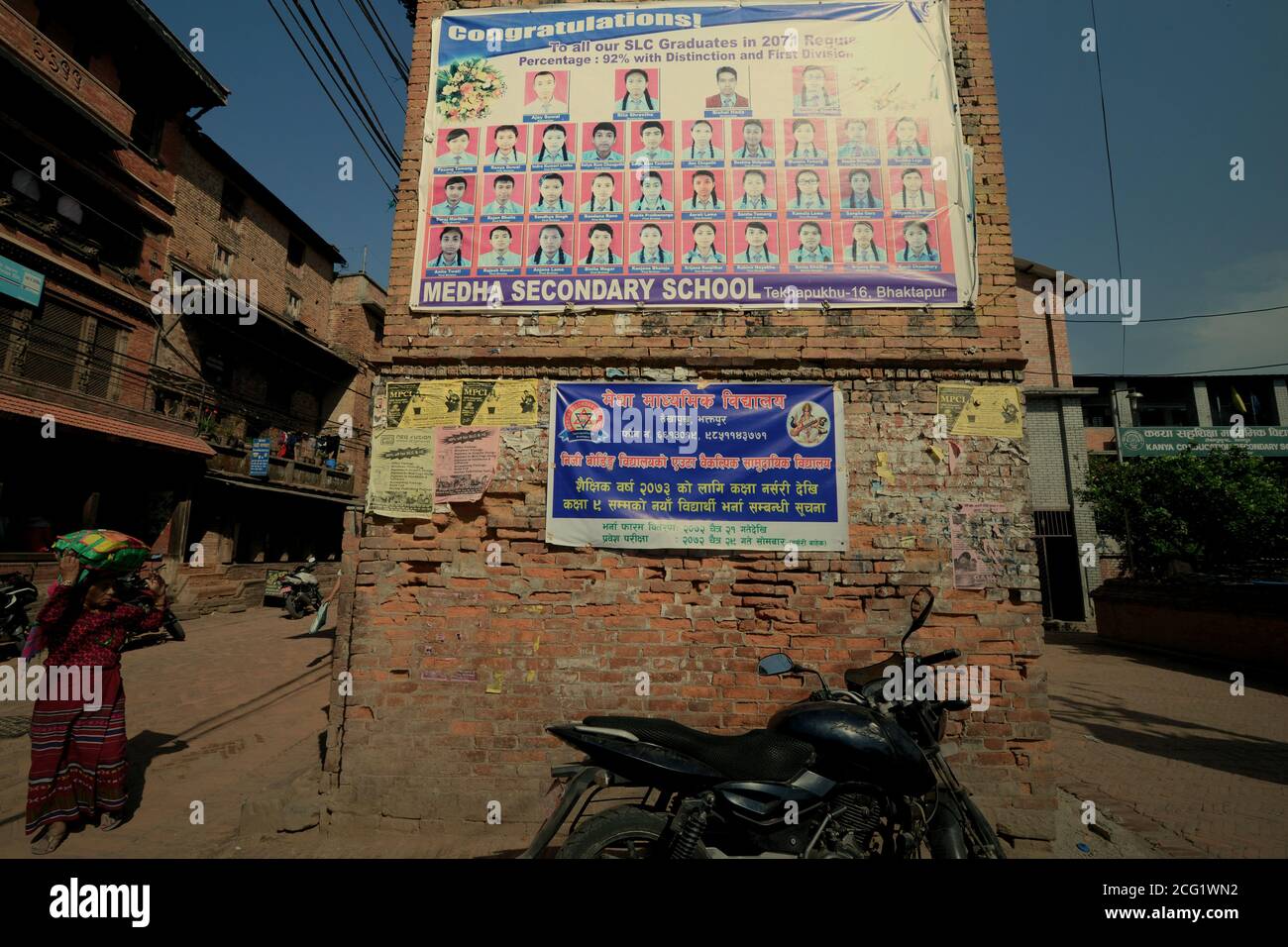 Une femme marchant dans une rue, près d'une affiche de remise des diplômes placée à la cour avant d'un bâtiment d'école secondaire à Bhaktapur, au Népal. Banque D'Images