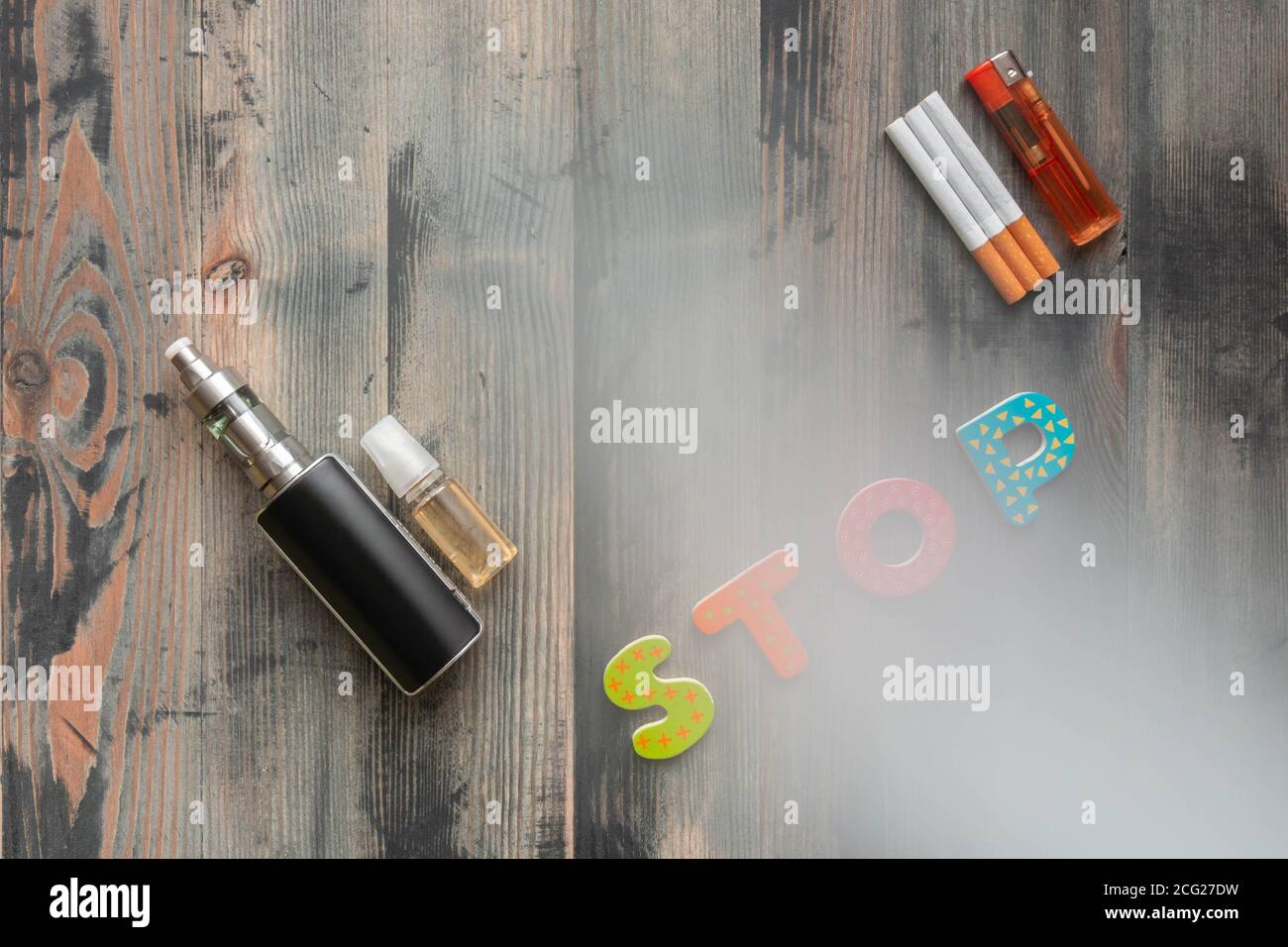 E-cigarette noire, e-liquide doux, cigarettes de tabac avec briquet et arrêt de mot de lettres en bois sur fond de bois gris fumée couverte. Vue de dessus. Banque D'Images