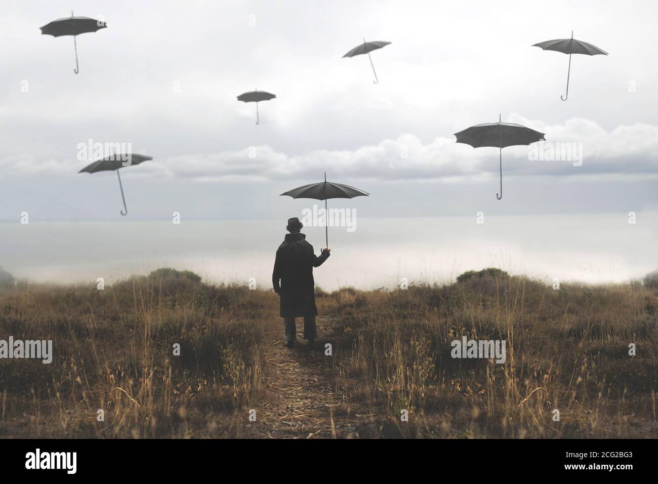 un homme solitaire avec un parapluie descend une route vers le le lac et les parasols noirs surréalistes volent dans le ciel Banque D'Images