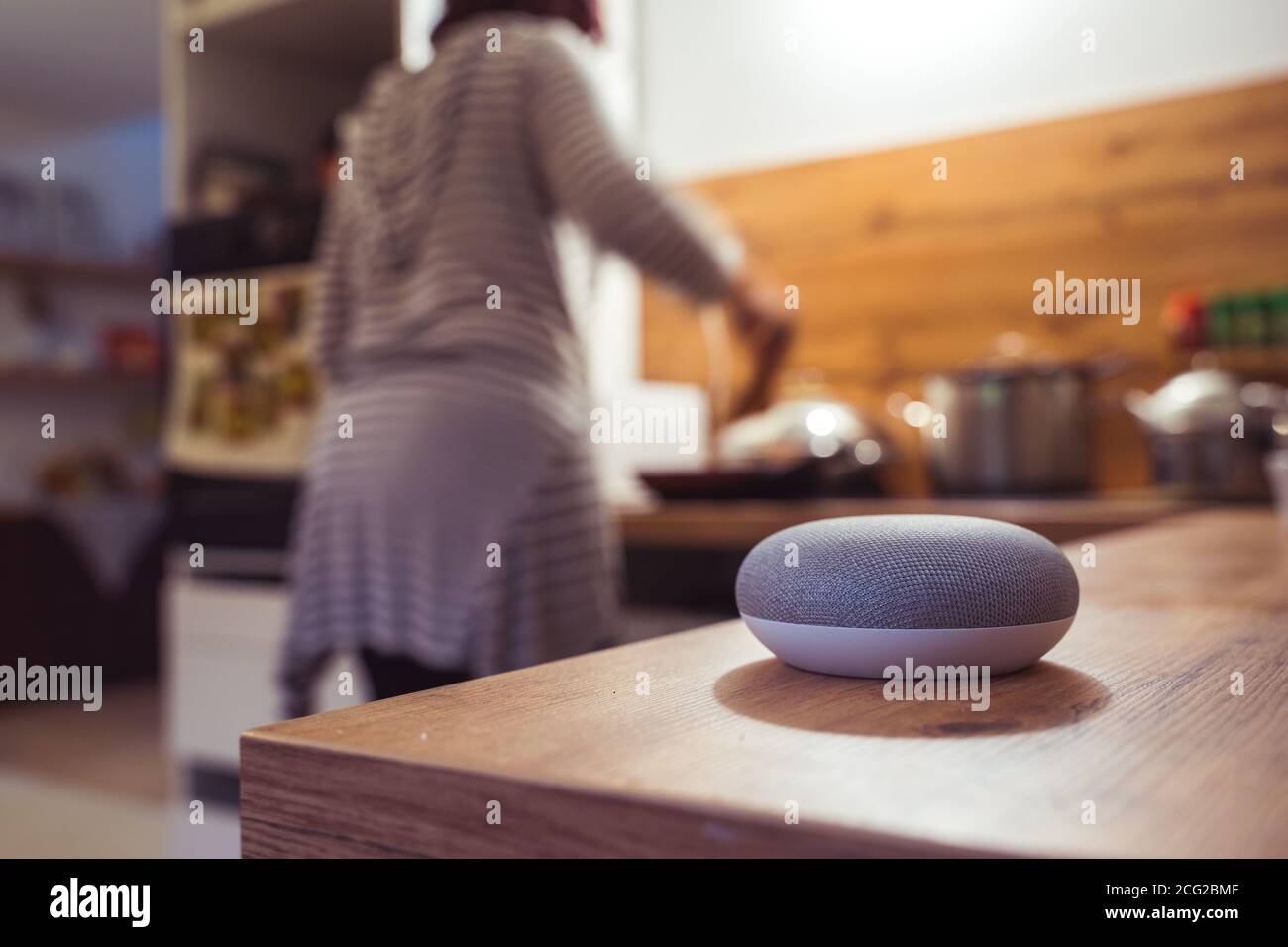 enceinte intelligente à commande vocale dans un intérieur à commande vocale enceinte intelligente dans un environnement intérieur avec une femme cuisiner en arrière-plan Banque D'Images