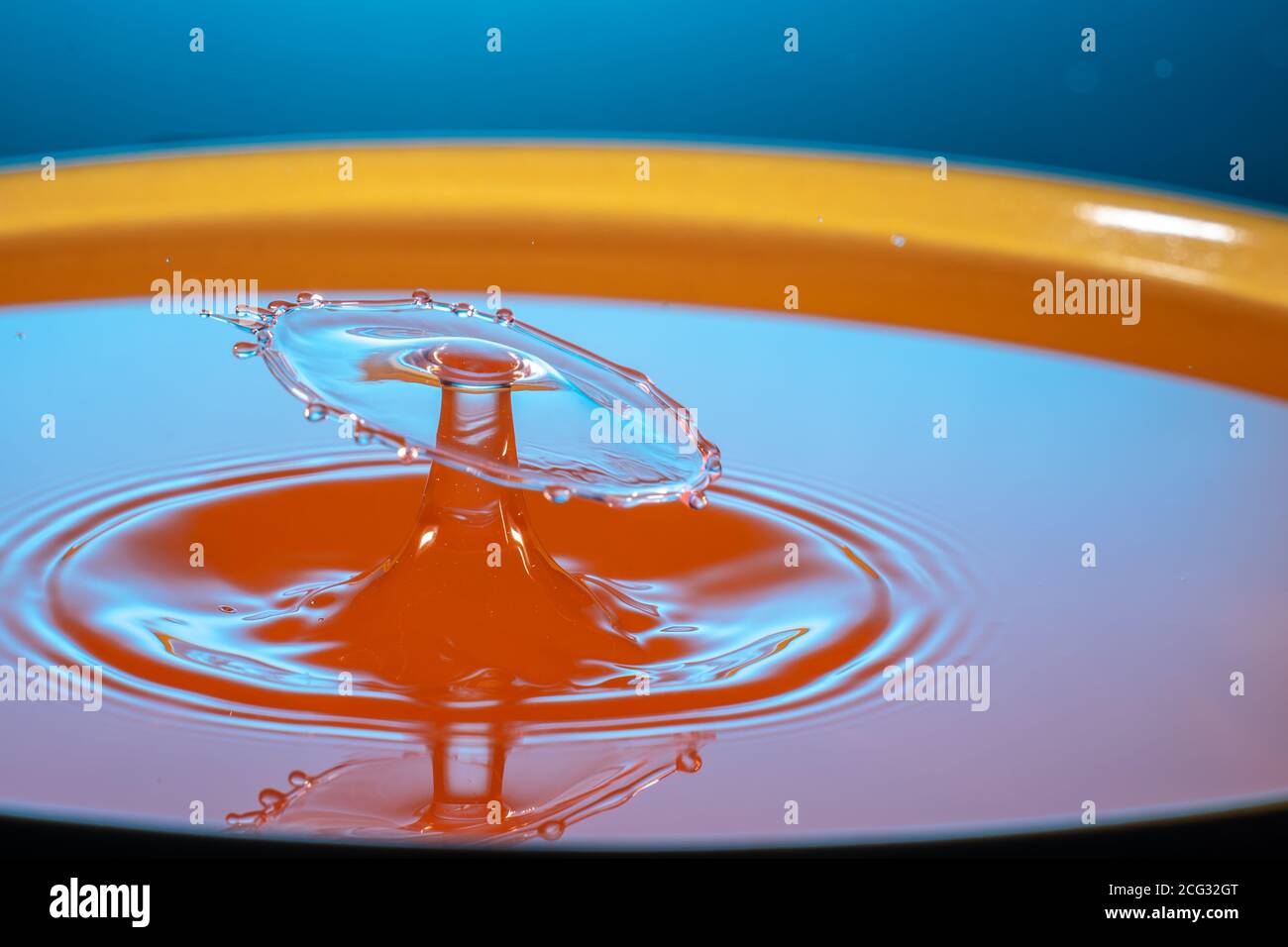 Deux gouttes de liquide orange tombent dans la tasse se frappant l'une l'autre puis la surface liquide est en forme de champignon Banque D'Images