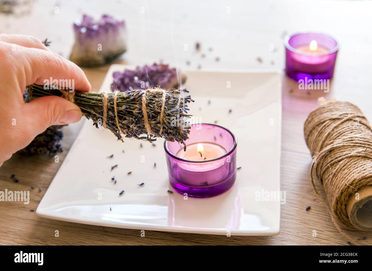 Personne tenant des herbes maison lavande (lavendula) bâton de taches avec la fumée sortant, des bougies et des amas de cristal améthyste pour la décoration. Banque D'Images