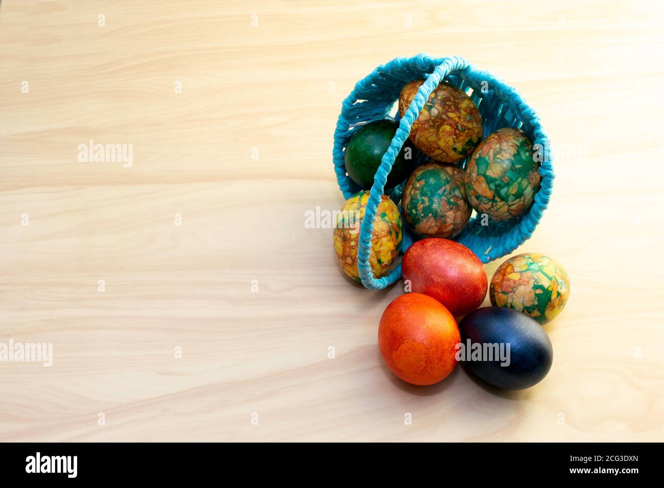 Oeufs de Pâques couchés sur la table en bois jaune et dans un panier bleu, pâtes de copie Banque D'Images