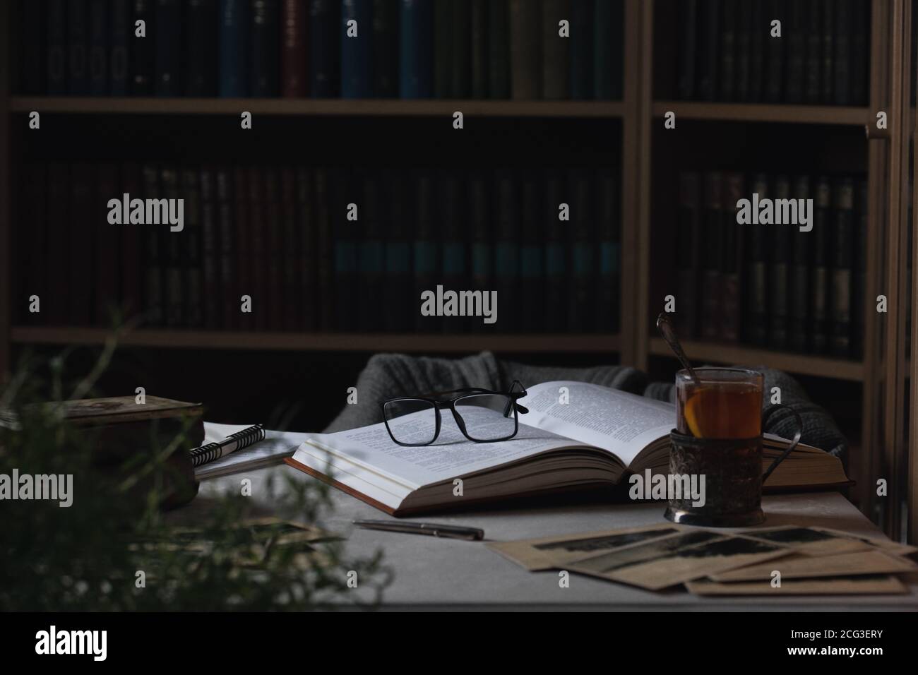Lunettes sur le livre ouvert et une tasse de thé. Bibliothèques en arrière-plan Banque D'Images