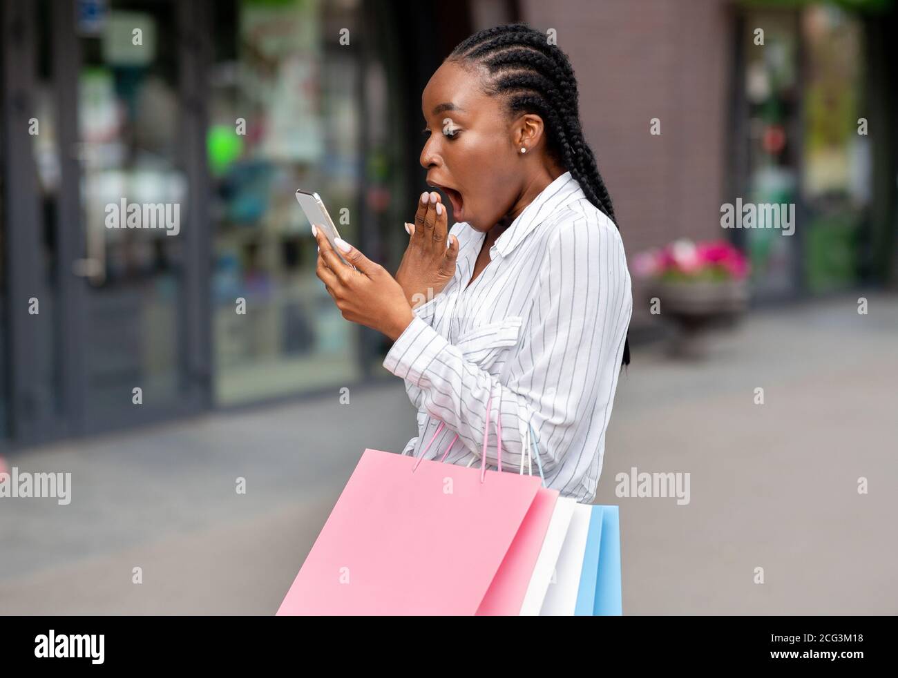 Annonce de remises importantes sur les applications mobiles. Une fille afro-américaine choquée avec des sacs a reçu un message sur son smartphone Banque D'Images