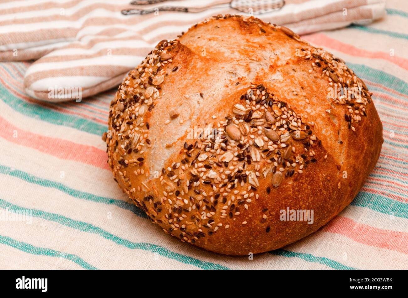 Pain de grain entier fraîchement cuit, parsemé de graines de lin, de sésame, de graines de tournesol sur une serviette en lin. Concept de cuisson maison saine. Gros plan Banque D'Images