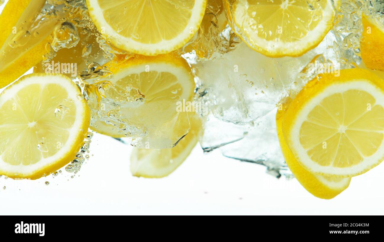 Tranches de citron avec des glaçons tombant profondément sous l'eau isolée sur fond blanc Banque D'Images