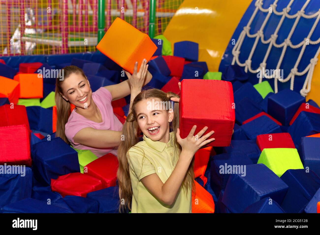 Bonne mère et fille qui se jettent des cubes doux les uns sur les autres au centre de divertissement pour enfants, à l'intérieur Banque D'Images