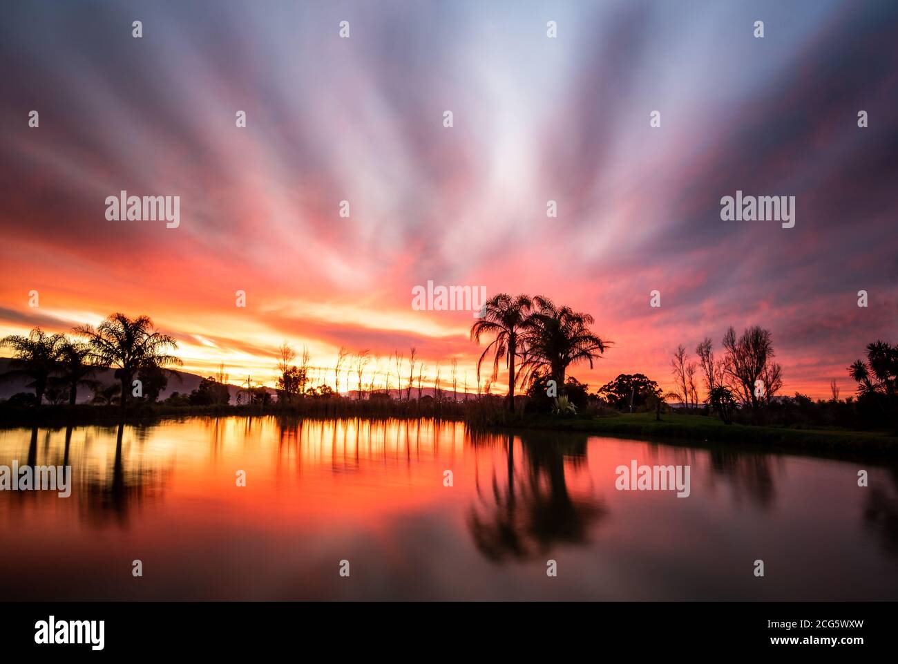Nuages sur feu pendant l'heure d'or avec ciel moody, réflexions sur la surface du barrage de ferme Banque D'Images