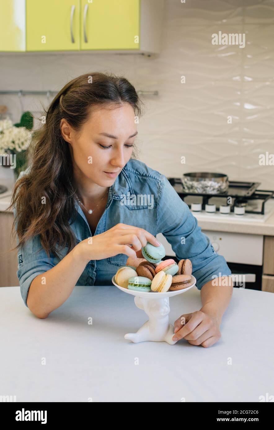 Femme assise dans une cuisine en choisissant un macaron Banque D'Images