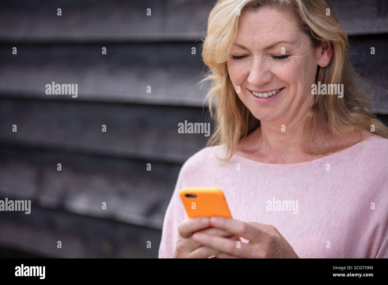 Portrait extérieur d'une jolie femme blonde d'âge moyen souriante utilisation d'un téléphone mobile pour la messagerie texte ou les réseaux sociaux Banque D'Images