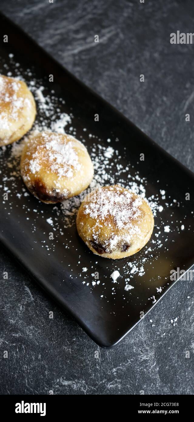 gâteau de bomboloni ou beignets avec sucre en poudre saupoudrés et servis sur une plaque noire et un tampon à pierres Banque D'Images