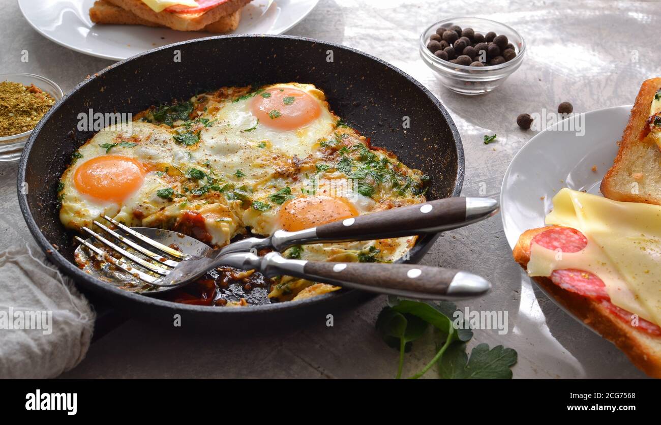 oeufs frits avec tomates, oignons et persil dans une casserole. Toast au fromage et à la saucisse. Petit déjeuner savoureux. Arrière-plan clair. Shakshuka. Banque D'Images