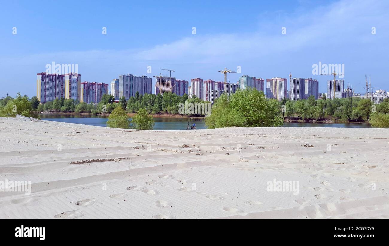 Vélo pliant debout sur la banque de sable déserte vide du lac avec vue sur la ville d'un nouveau quartier avec des grues de construction près de blocs de haute élévation. Banque D'Images