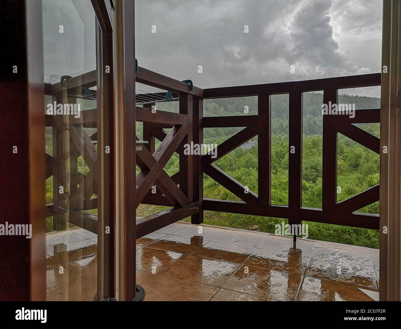 Vue à travers la porte du balcon ouverte sur les nuages gris orage au-dessus de la forêt et des montagnes. Balcon avec rampes en bois. Temps sombre nuageux le jour. Banque D'Images