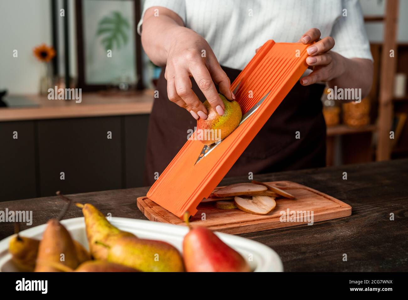 Gros plan d'une femme méconnue qui fait des tranches de poire à l'aide d'un trancheuse à mandoline tout en cuisinant dans la cuisine Banque D'Images
