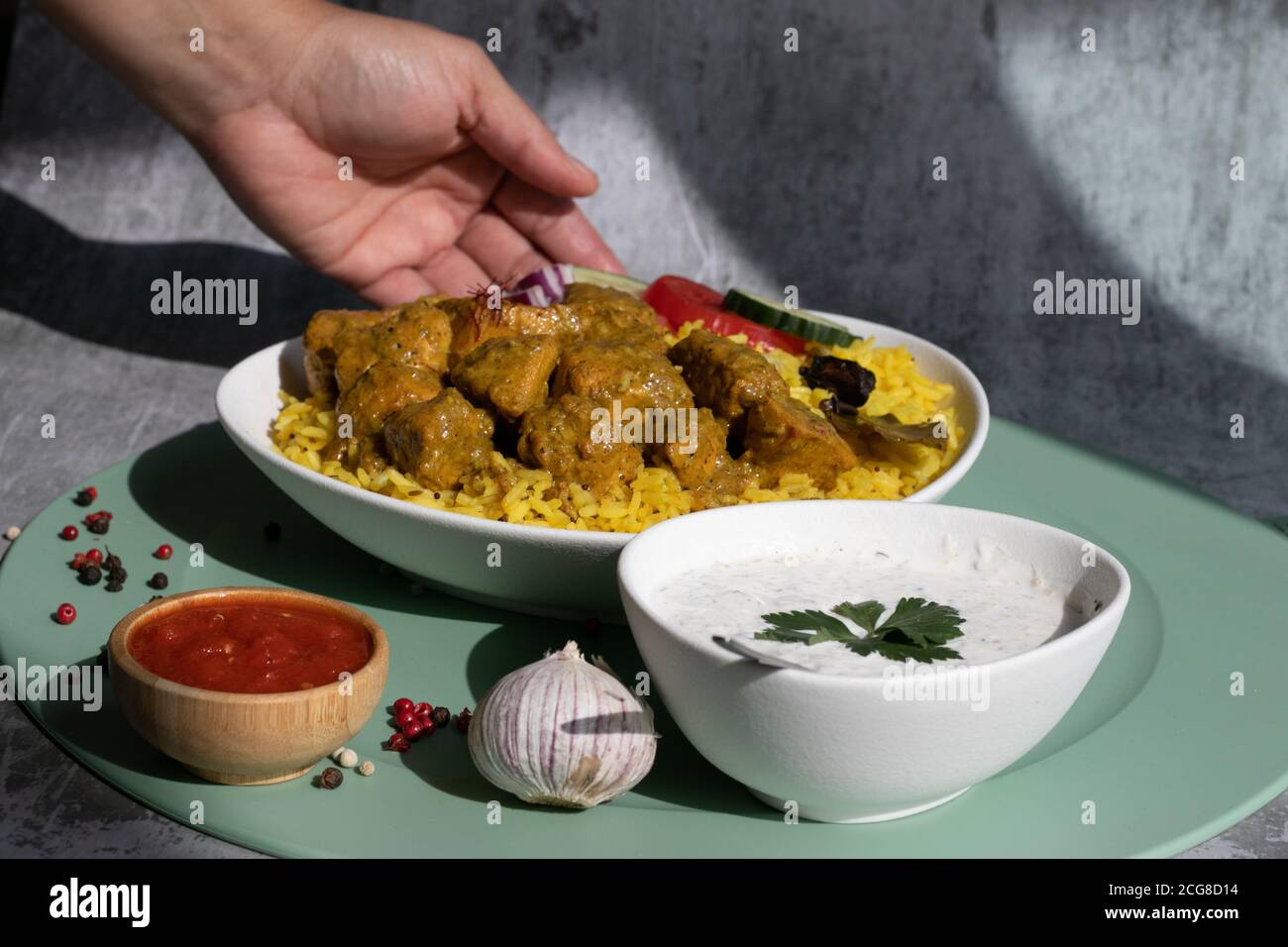 Assiette de curry avec piment et yaourt, nourriture servie, main, fond gris et tapis vert Banque D'Images