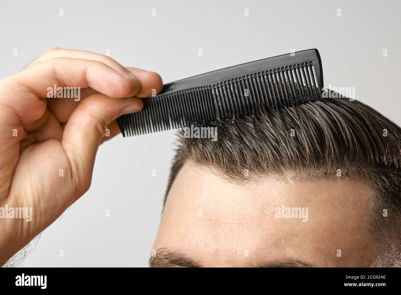 Gros plan homme se brossant ses cheveux avec un peigne en plastique sur  fond gris. Traitement contre la perte de cheveux et le concept de  pellicules. Produits cosmétiques pour hommes Photo Stock -