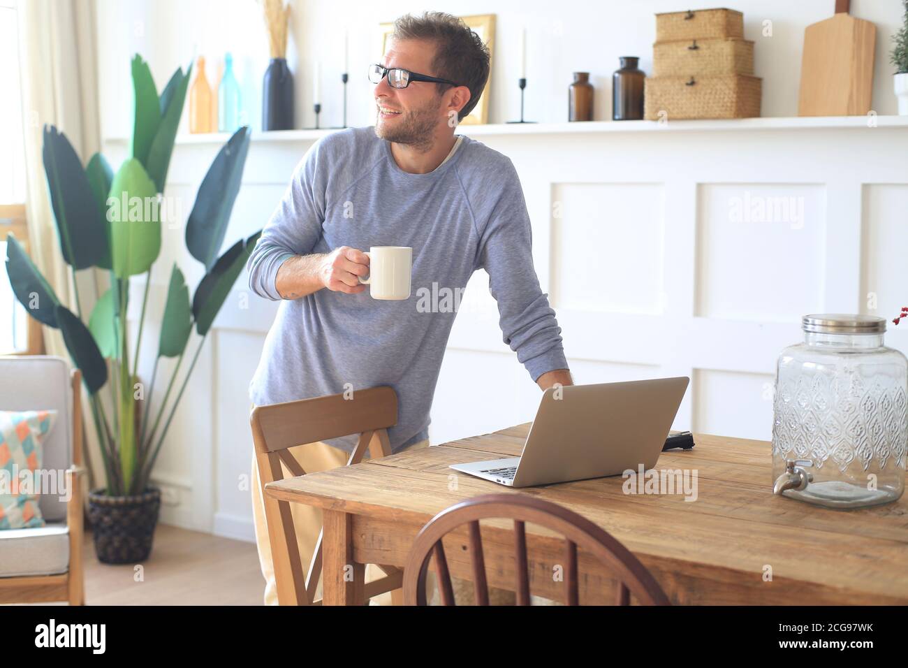 Un jeune homme avec une tasse de café travaille au table à la maison le matin Banque D'Images