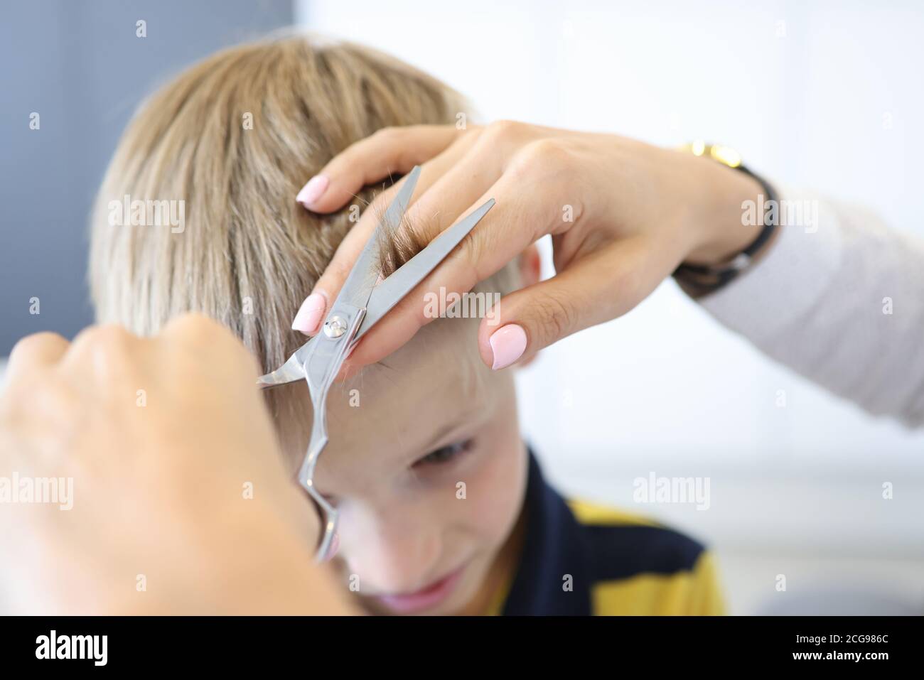 Le coiffeur principal coupe les langes du garçon blond. Banque D'Images