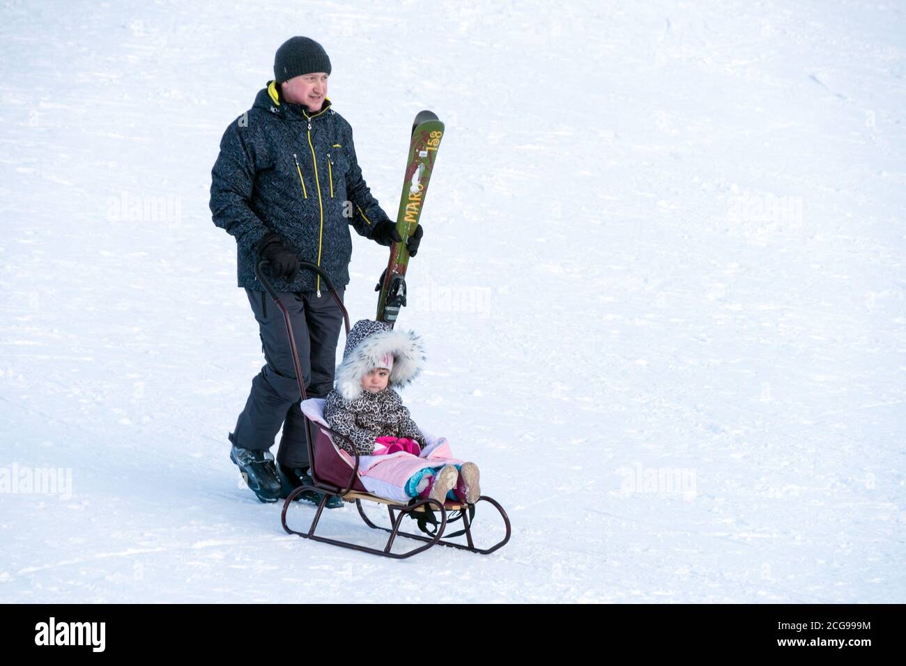 Le père roule sa fille sur un traîneau sur le flanc de la montagne. Banque D'Images