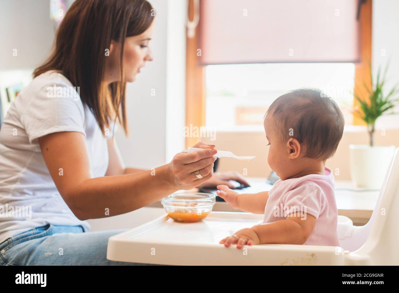 Mère nourrir sa petite fille avec une cuillère et chercher sur internet des recettes de nourriture Banque D'Images