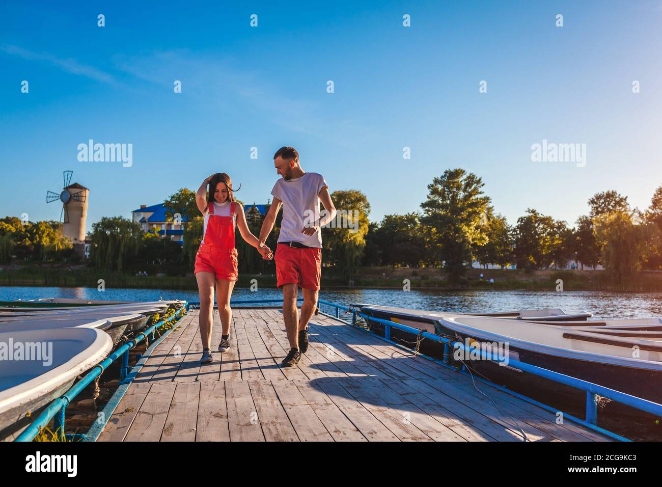 Un jeune homme et une jeune femme qui court le long du quai de la rivière d'été. Couple s'amusant au coucher du soleil en tenant les mains. Les gens se détendent Banque D'Images