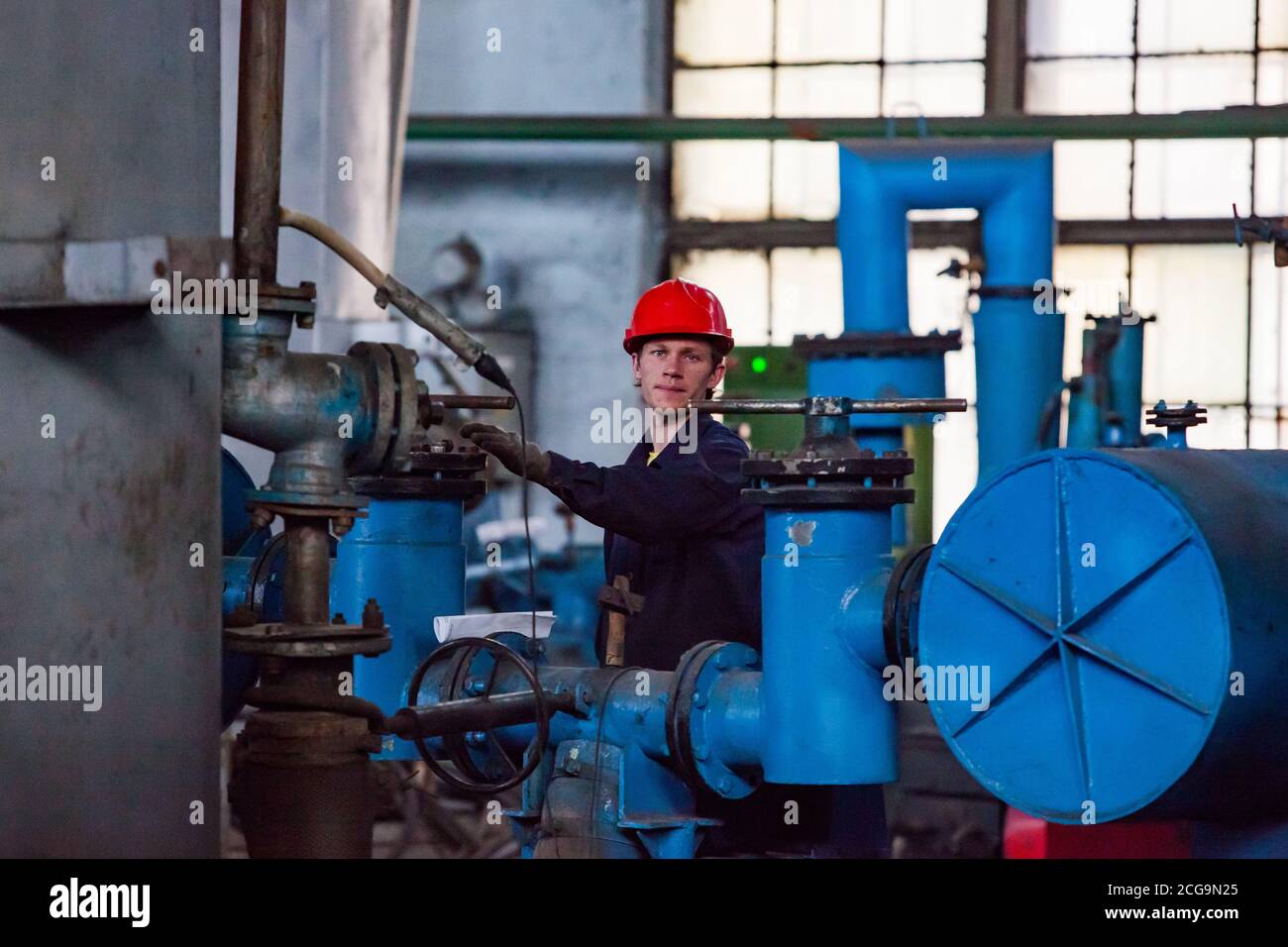 Usine de métallurgie du titane. Jeune métallurgiste près d'un four sous vide. Tube gris et équipement bleu. Banque D'Images