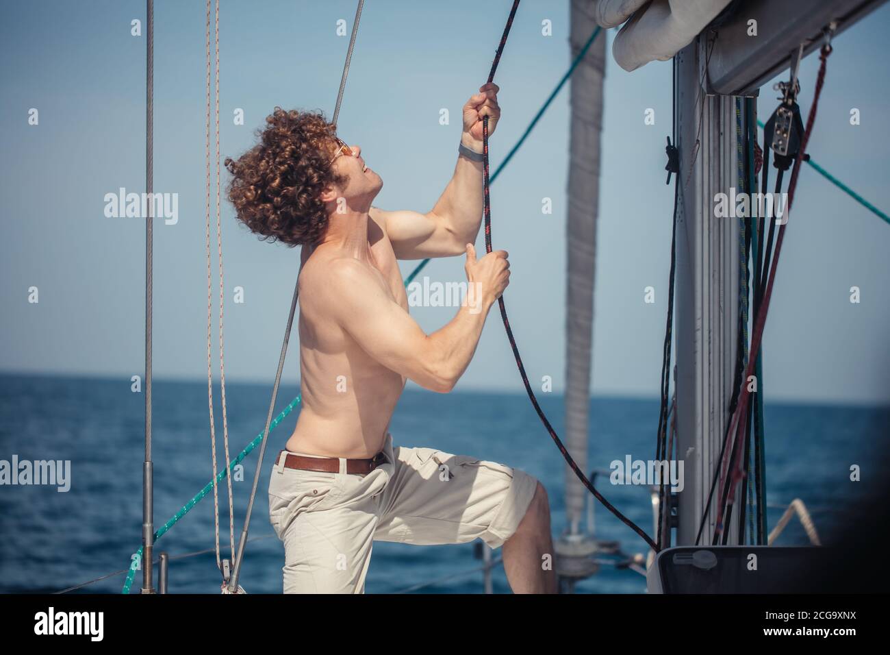 Jeune hadsome hippster marin homme avec des poils flous voile un bateau pour emmener ses amis à un voyage en mer, tirant la corde Banque D'Images