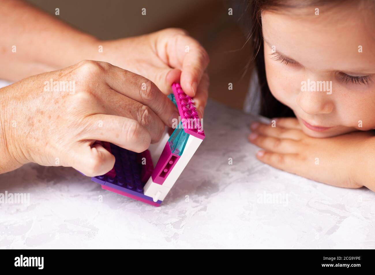 Enfant de 5 ans, une fille observe que les mains de sa grand-mère collectent les détails du constructeur, gros plan Banque D'Images